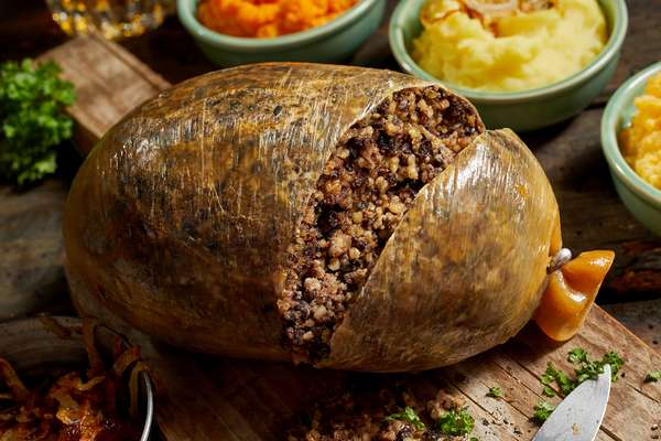 Close up on a sliced open cooked haggis. Close up on a sliced open cooked Scottish haggis on a cutting board with side dishes of potato, turnips and carrot.