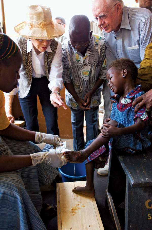 At Savelugu Hospital in Northern Region, Ghana, former U.S. President Jimmy Carter and his wife, Rosalynn, watch as a Guinea worm health worker dresses a child's extremely painful Guinea worm wound.